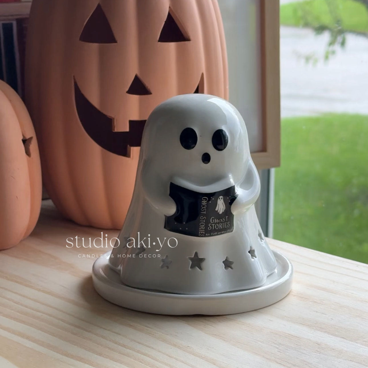 Ghost-shaped candle holder on a wooden surface with pumpkins in the background