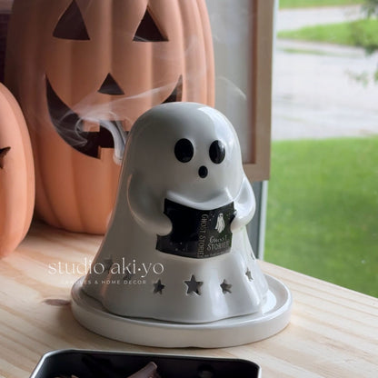 Ghost-shaped diffuser with smoke emitting from it, placed on a surface with pumpkins in the background.