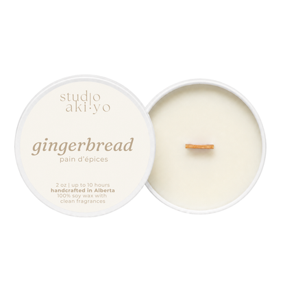 A round soy wax candle shown open with the cream-colored lid beside it on a white background. The lid reads 'studio aki·yo gingerbread pain d’epices' and the wax inside has a small wooden wick.