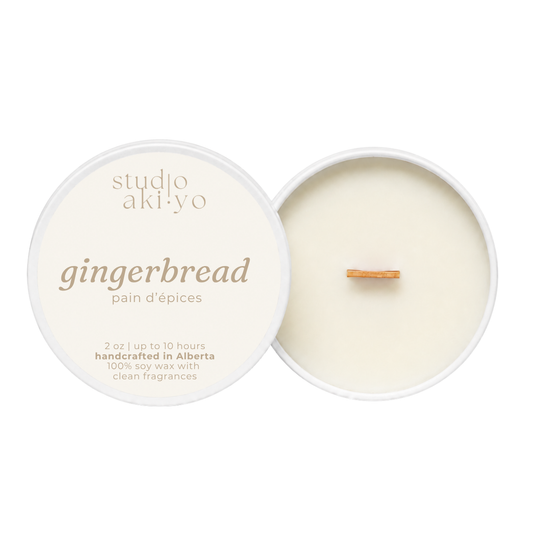 A round soy wax candle shown open with the cream-colored lid beside it on a white background. The lid reads 'studio aki·yo gingerbread pain d’epices' and the wax inside has a small wooden wick.