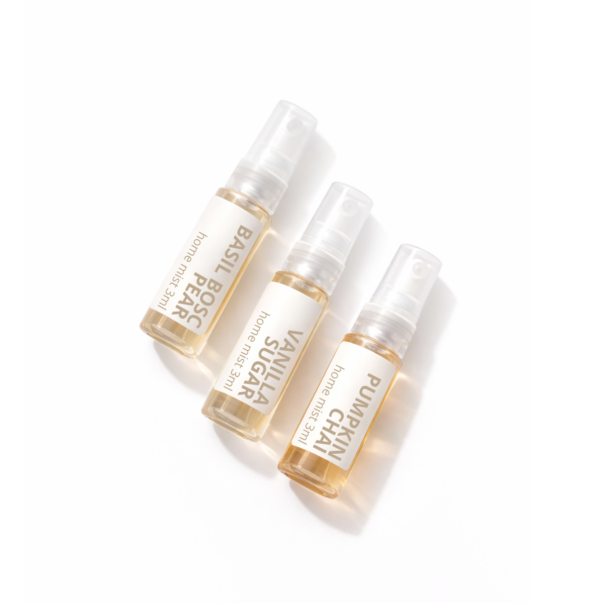 Three small home fragrance spray bottles arranged diagonally on a clean white background. The bottles contain a pale golden liquid and are labeled Basil Boss Home Fragrance, Vanilla Sugar Home Fragrance, and Pumpkin Chai Home Fragrance.