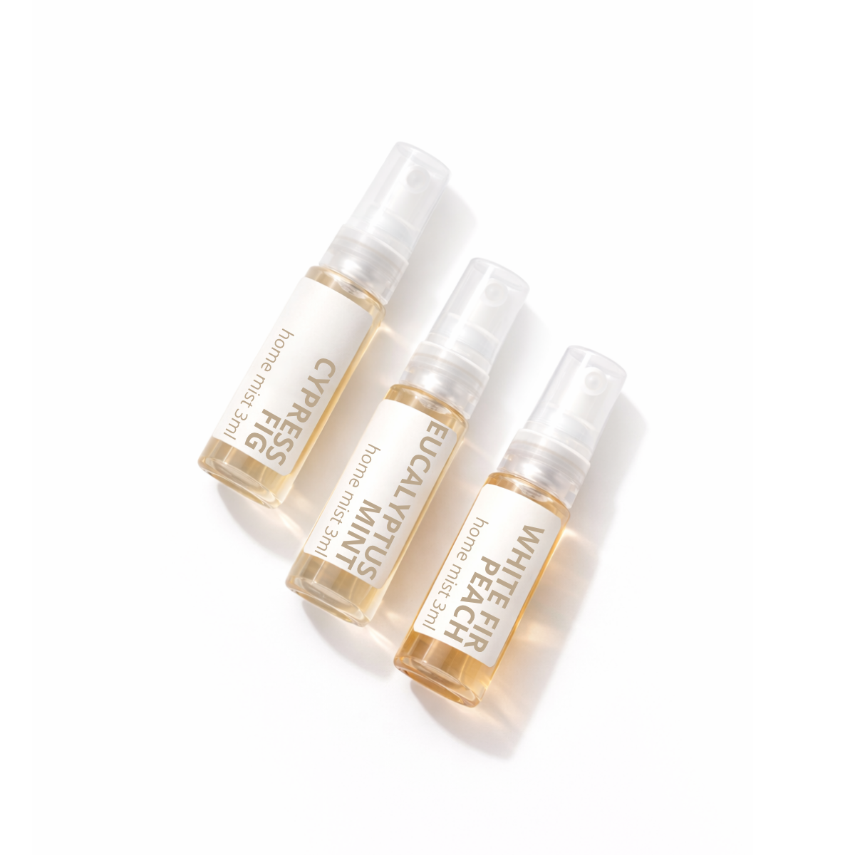 Three small home fragrance atomizer bottles with clear caps and white labels, arranged diagonally on a clean white background. The labels read 'home mist spray' and show scents including Cypress Egg Mint, Elucidated Yachtus Mint, and White Peach.