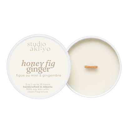 A round soy wax candle shown open with its lid beside it on a white background. The lid is cream-colored with brown text reading 'studio akiyo honey fig ginger.