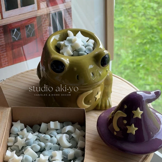Magical toad wax warmer with wax melts and a purple witch hat on a wooden surface, branded 'studio akiyo'.