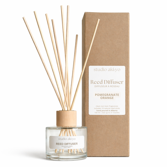 Pomegranate Orange Studio Akiyo reed diffuser with wooden sticks and a cardboard on a white background.