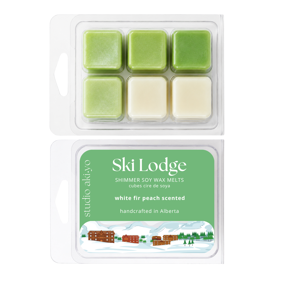 Two packaged wax melts on a white background: an open clear clamshell showing six square wax cubes in light green and creamy off-white, and a matching closed package labeled Ski Lodge by studio aldiyo with green text panel and winter illustration.