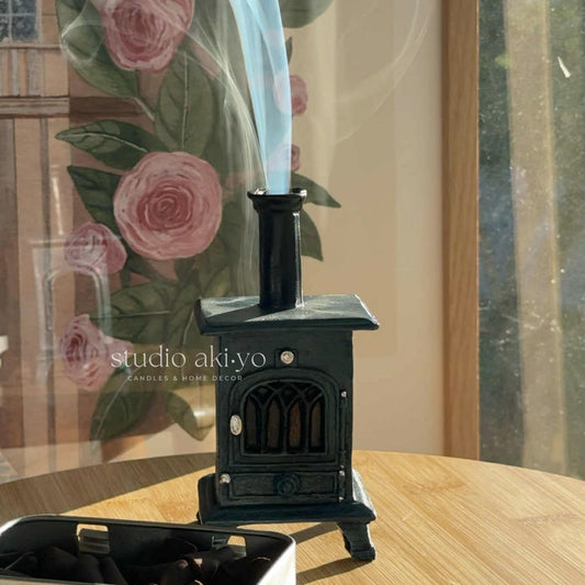 Small black stove incense cone holder on a wooden surface with floral curtains in the background