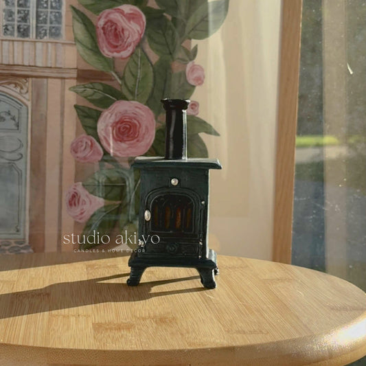Small black stove incense cone holder on a wooden surface with floral curtains in the background