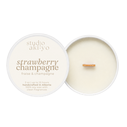 An open round soy wax candle labeled 'studio aki yo strawberry champagne' with cream-colored wax and a small cinnamon stick wick, shown on a white background.