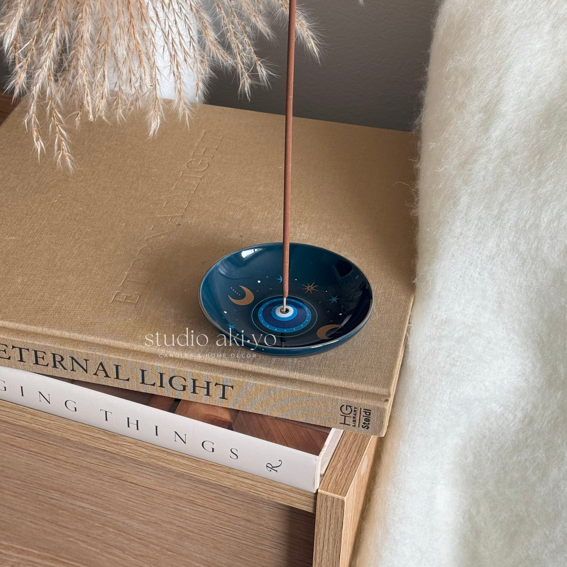 Incense stick holder in a blue all seeing eye print dish on top of books with a soft background