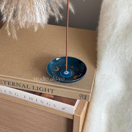 Incense stick holder in a blue all seeing eye print dish on top of books with a soft background