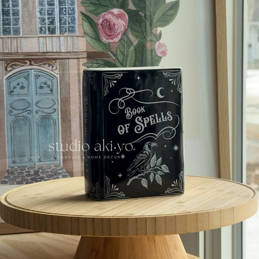 Decorative pot with 'Book of Spells' design on a wooden table, featuring the brand 'studio aki.yo'.