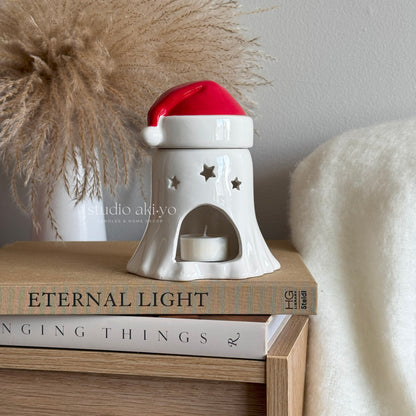 White ceramic candle holder with a red top on books, next to decorative pampas grass and a white blanket.