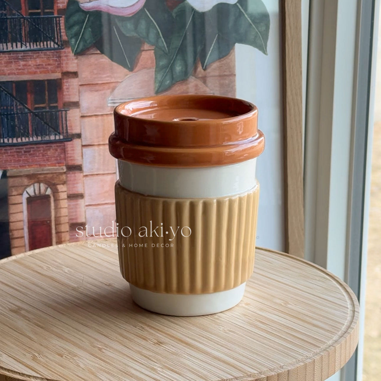 Brown and white ceramic cup with lid on a wooden surface, with 'studio akiyo' branding.