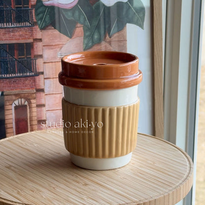 Brown and white ceramic cup with lid on a wooden surface, with 'studio akiyo' branding.