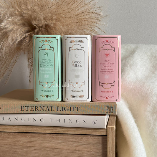 Three small books or boxes with decorative covers on a wooden surface, with a neutral background.