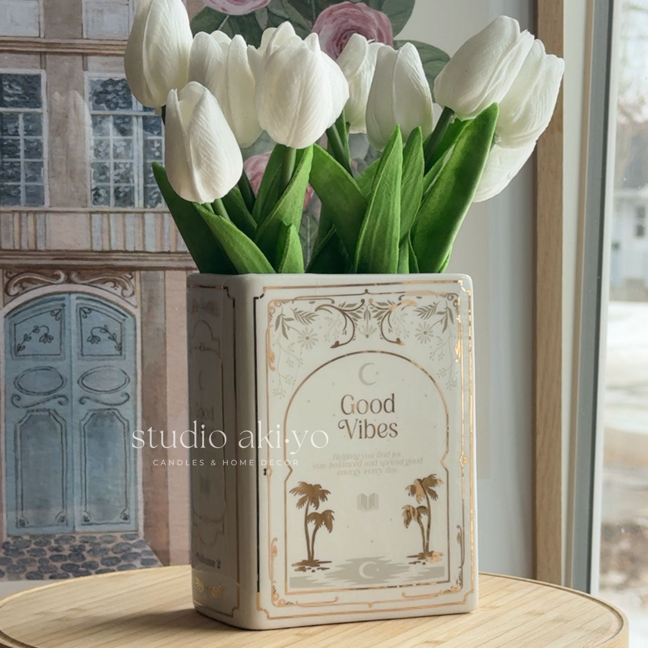 White tulips in a decorative vase with 'Good Vibes' text on a wooden surface.