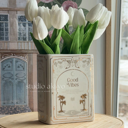 White tulips in a decorative vase with 'Good Vibes' text on a wooden surface.