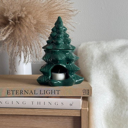 Green ceramic tree-shaped oil burner on a stack of books with a neutral background