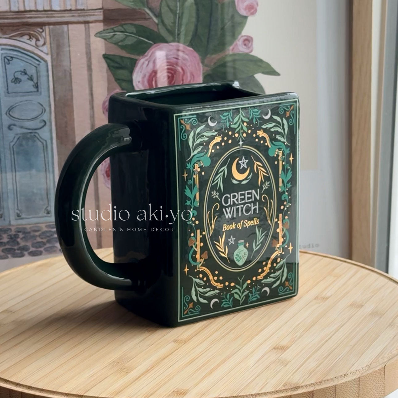 Black mug with 'Green Witch Book of Spells' design on a wooden surface