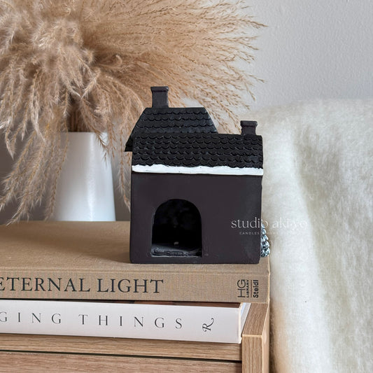 Black house-shaped candle on a stack of books with decorative elements in the background