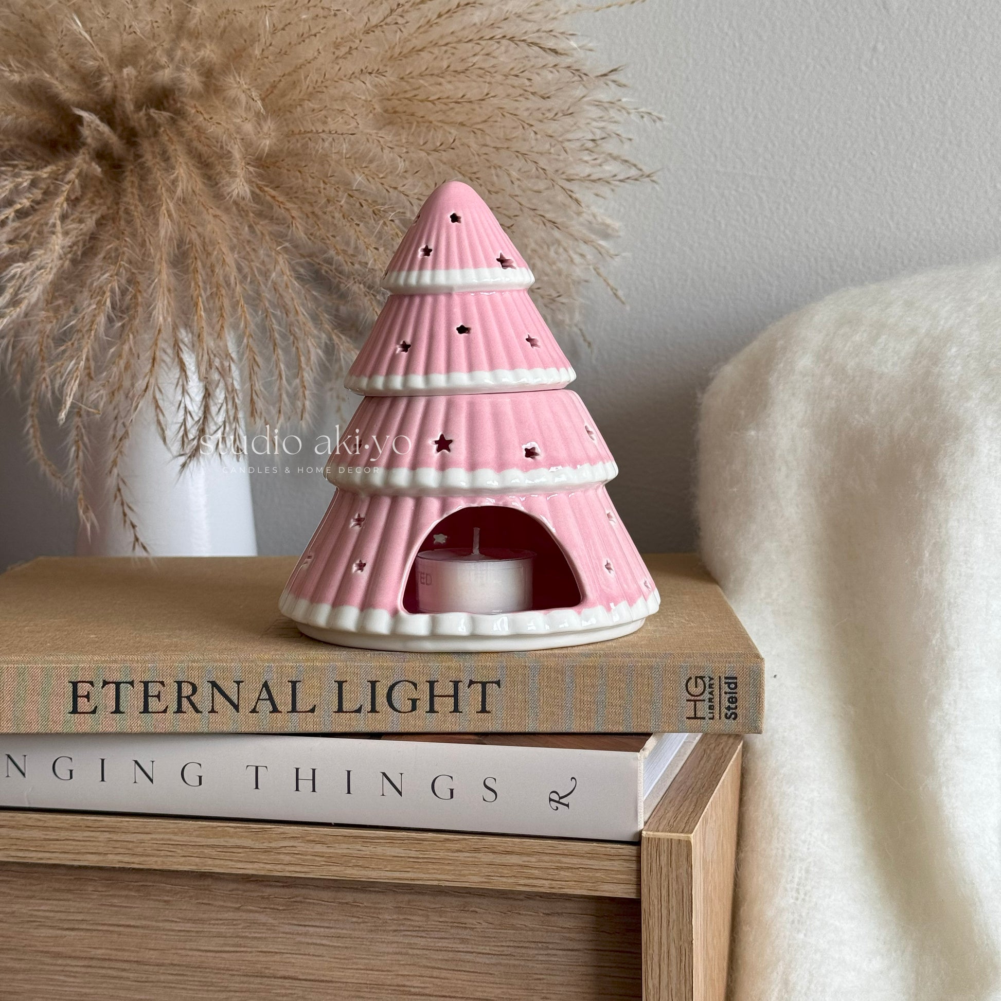 Pink ceramic tree-shaped lantern on books with a neutral background