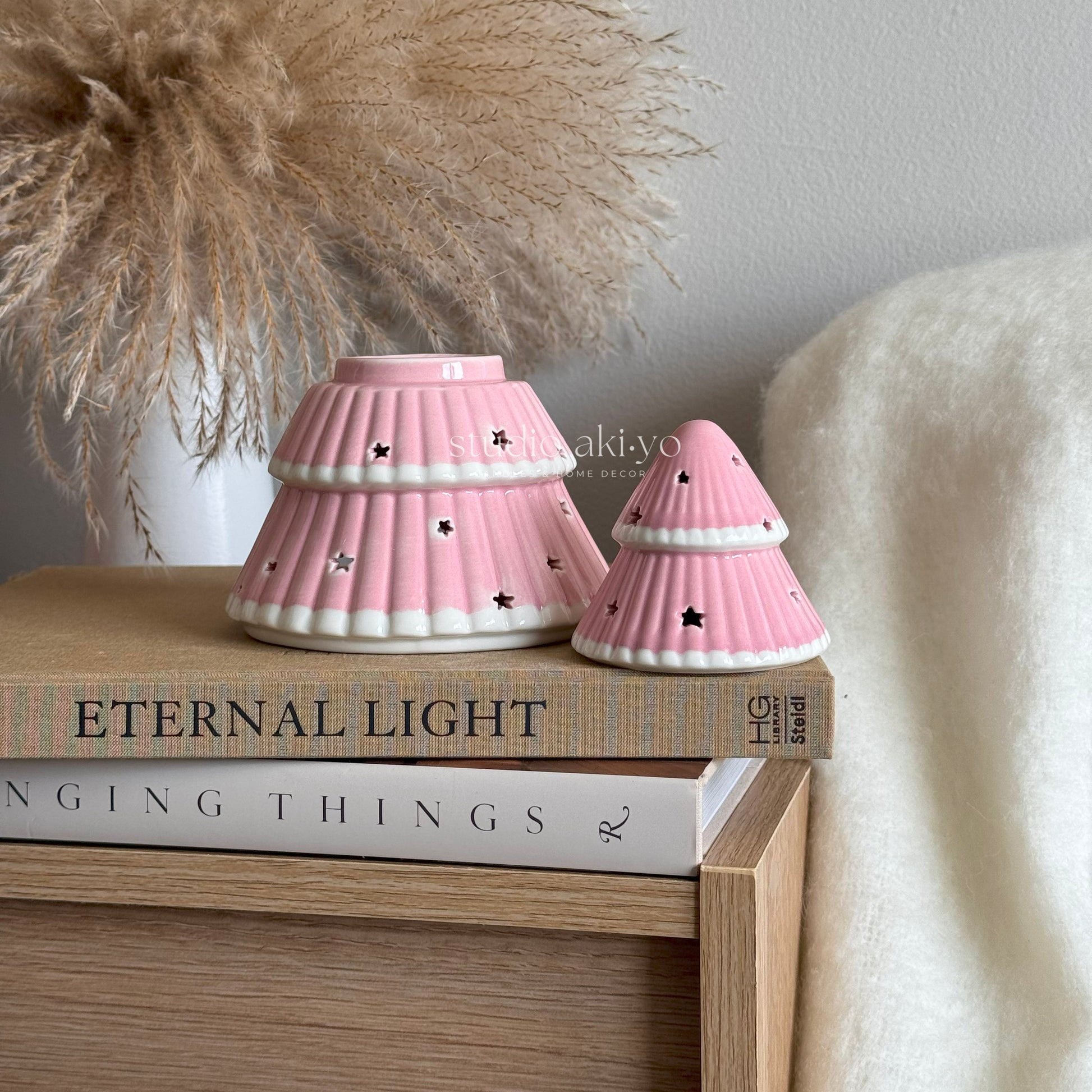 Two pink ceramic lamps on a stack of books with decorative elements in the background.