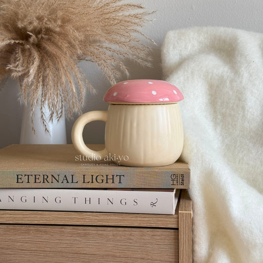 Beige mug with pink lid on books next to decorative pampas grass and white blanket