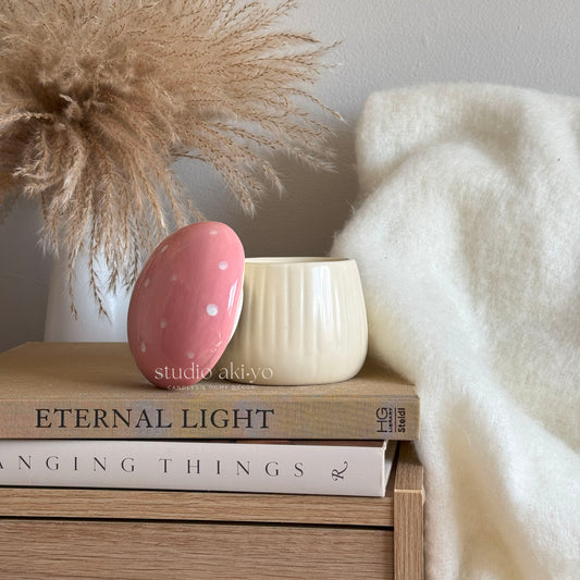 Pink ceramic egg with white polka dots on a stack of books with decorative elements.