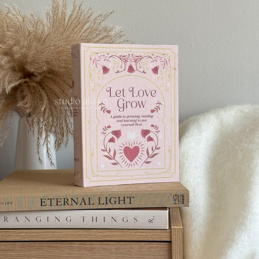 Book titled 'Let Love Grow' on a wooden surface with decorative elements.