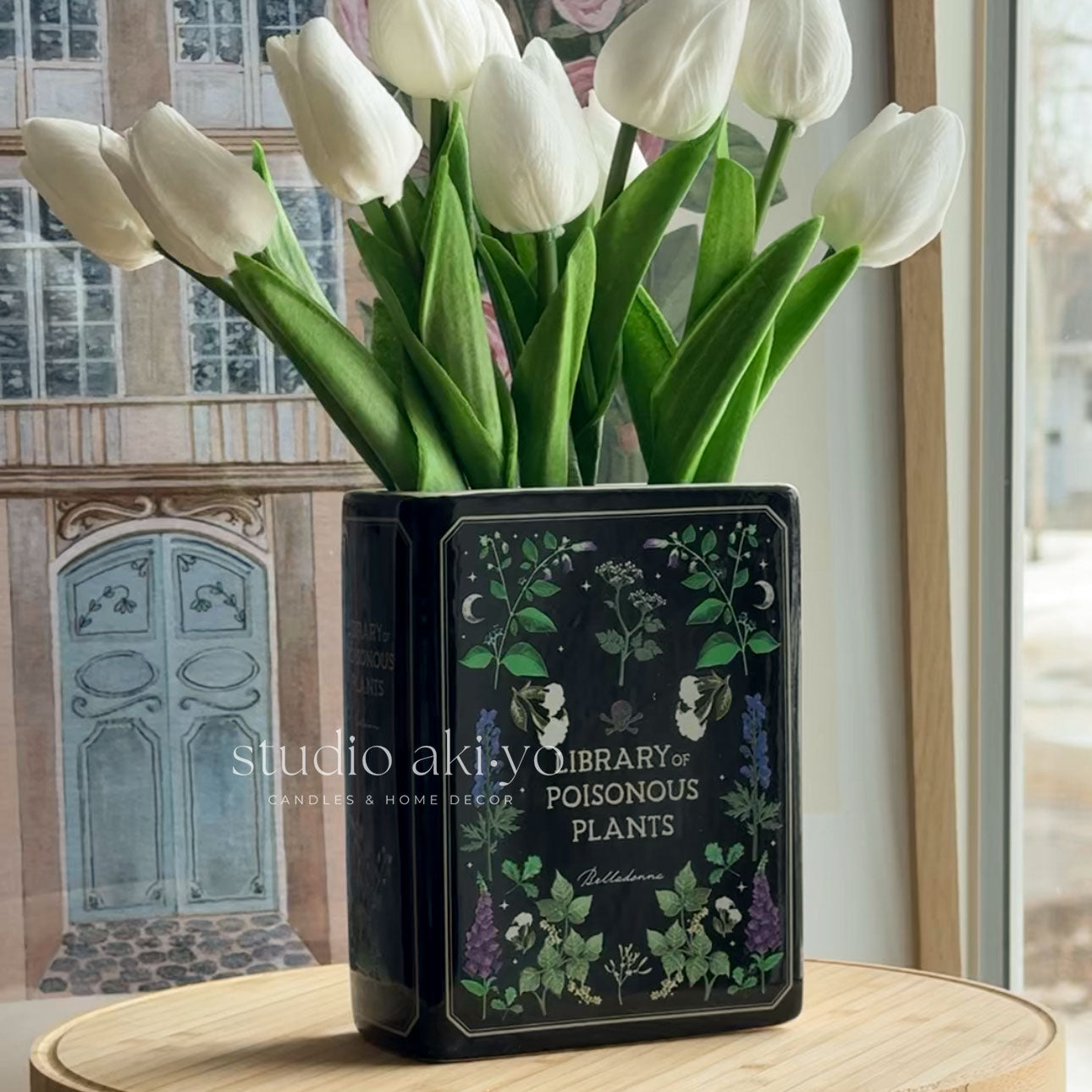 Vase with white tulips on a table in a room with large windows.