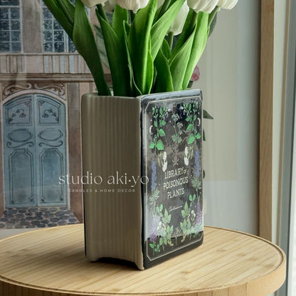 Decorative vase with book design containing white tulips on a wooden surface.