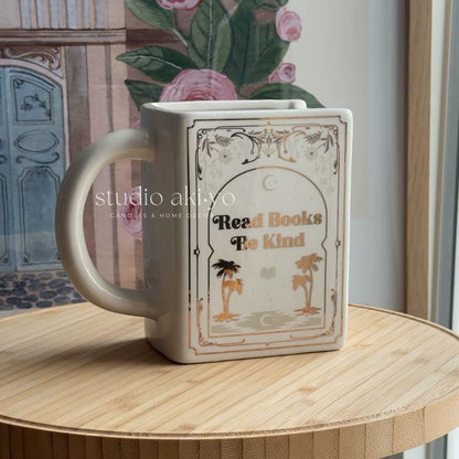 Mug with book design and 'Read Books To Kind' text on a wooden surface.