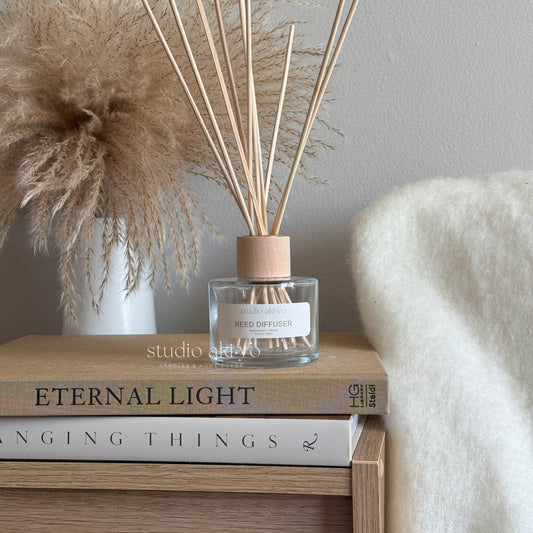 Clear glass reed diffuser with wooden cap and natural rattan reeds, styled on a neutral background. Minimalist home fragrance decor harvest scented