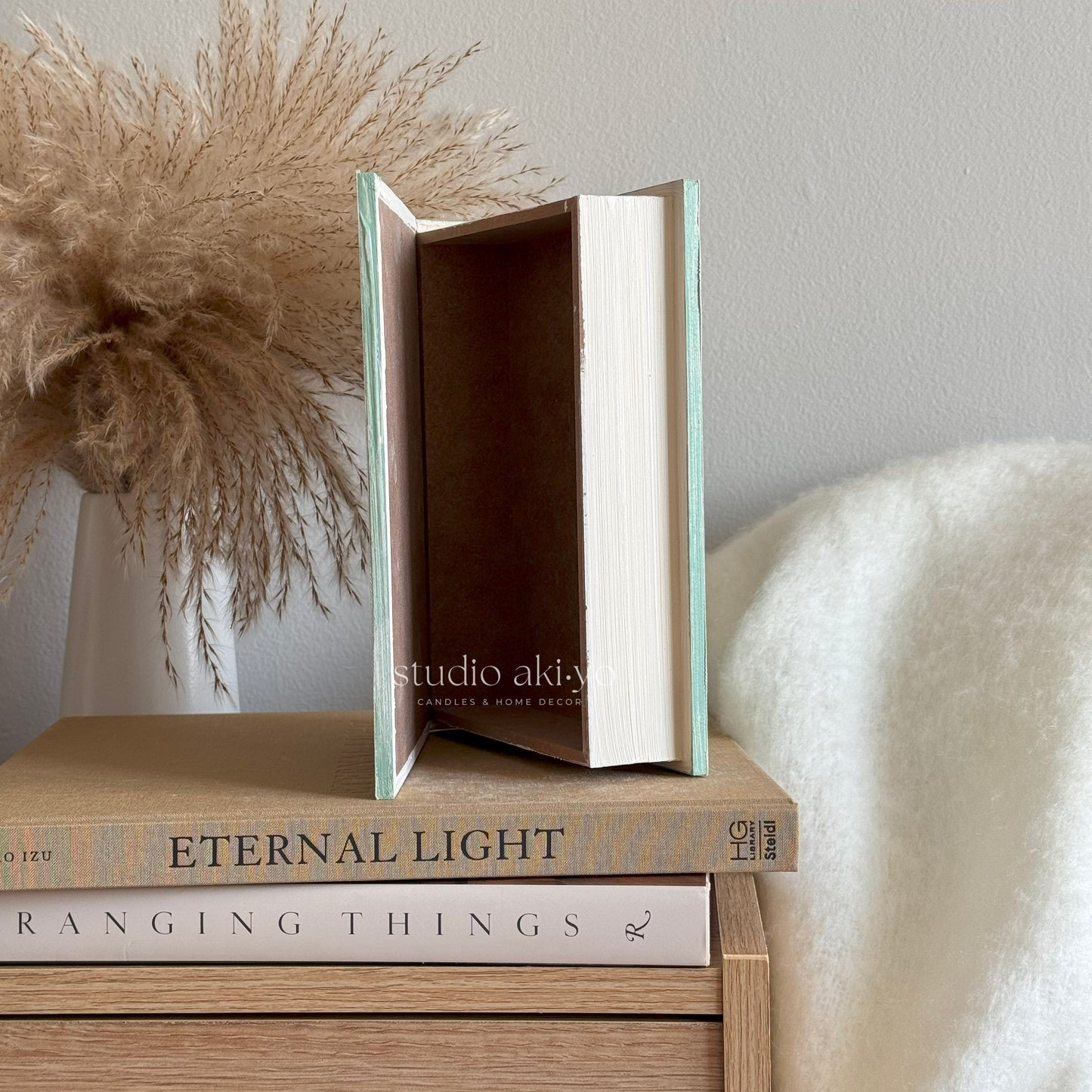 Stack of books with 'studio aki-y' on a wooden surface with decorative elements.