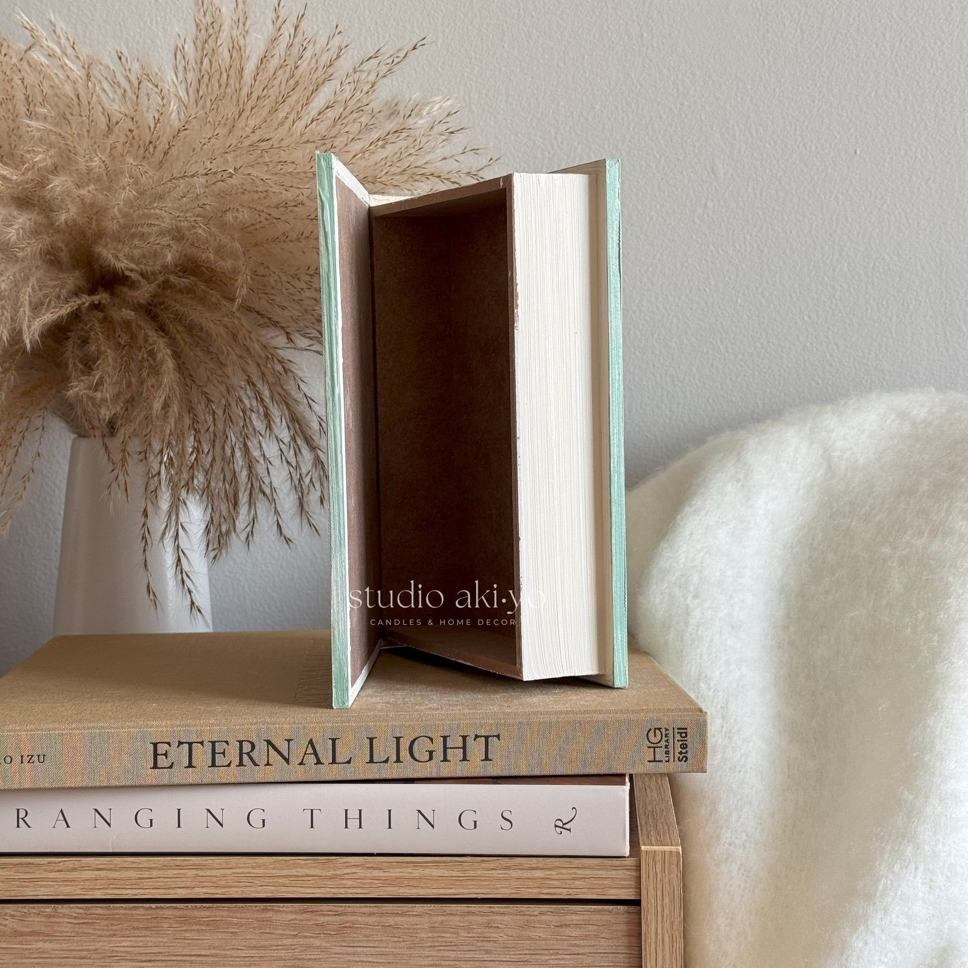 Stack of books with 'studio aki-y' on a wooden surface with decorative elements.