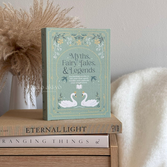 Book titled 'Myths, Fairy Tales, & Legends' on a wooden surface with decorative elements.