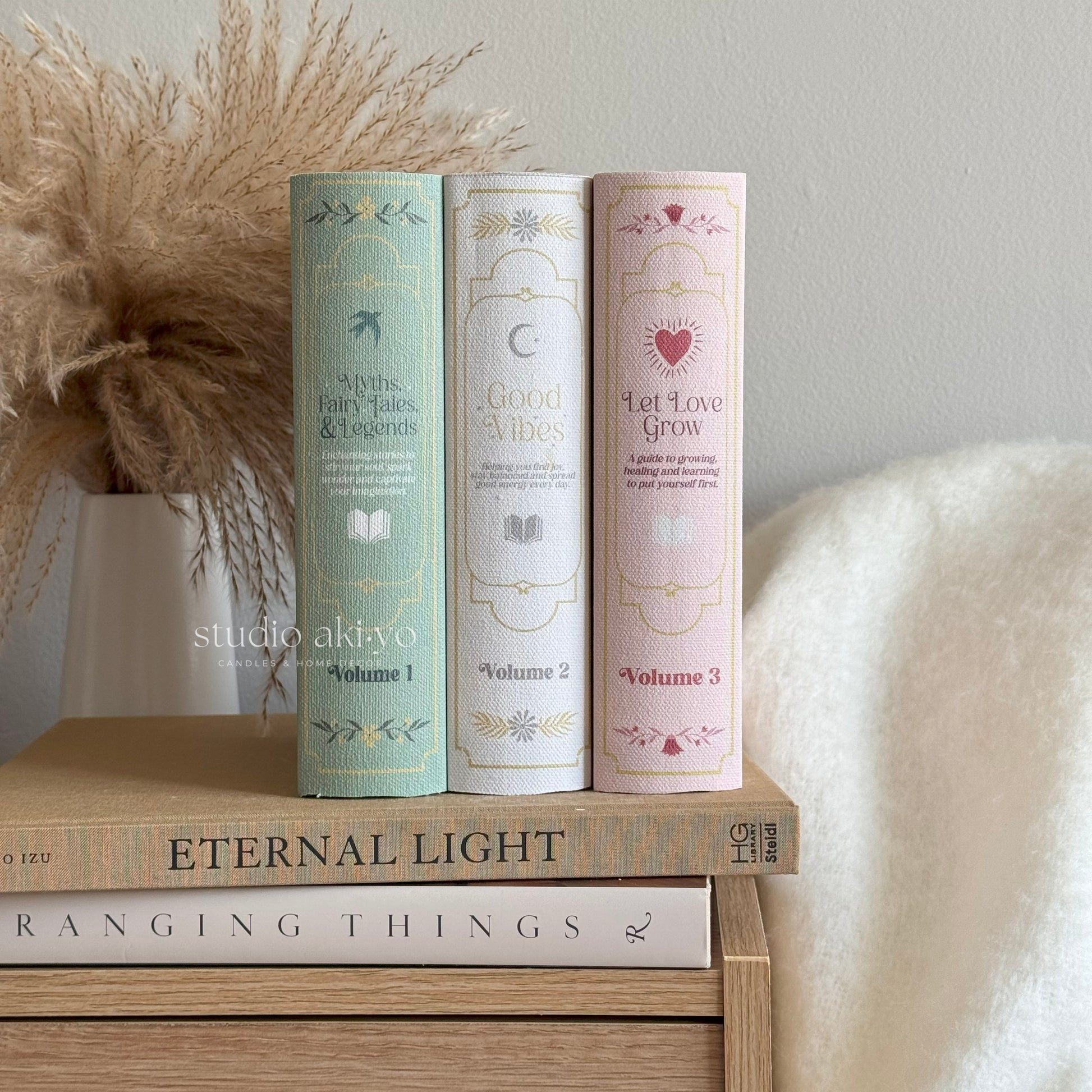 Three cylindrical books with decorative covers on a wooden surface, with 'studio akivo' branding.