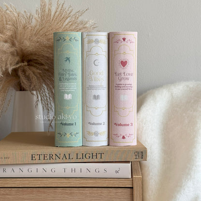 Three cylindrical books with decorative covers on a wooden surface, with 'studio akivo' branding.