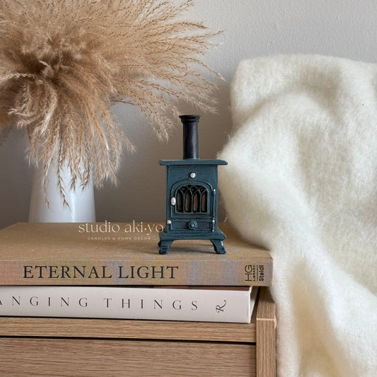 Small black stove incense cone burner on books with decorative elements like pampas grass and a white blanket.