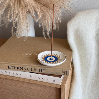 Incense stick on a decorative plate with books and pampas grass in the background