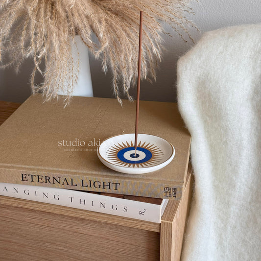Incense stick on a decorative plate with books and pampas grass in the background