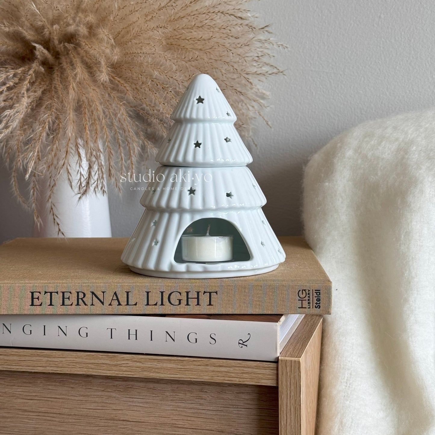 White ceramic tree-shaped candle holder on a stack of books with decorative items in the background.