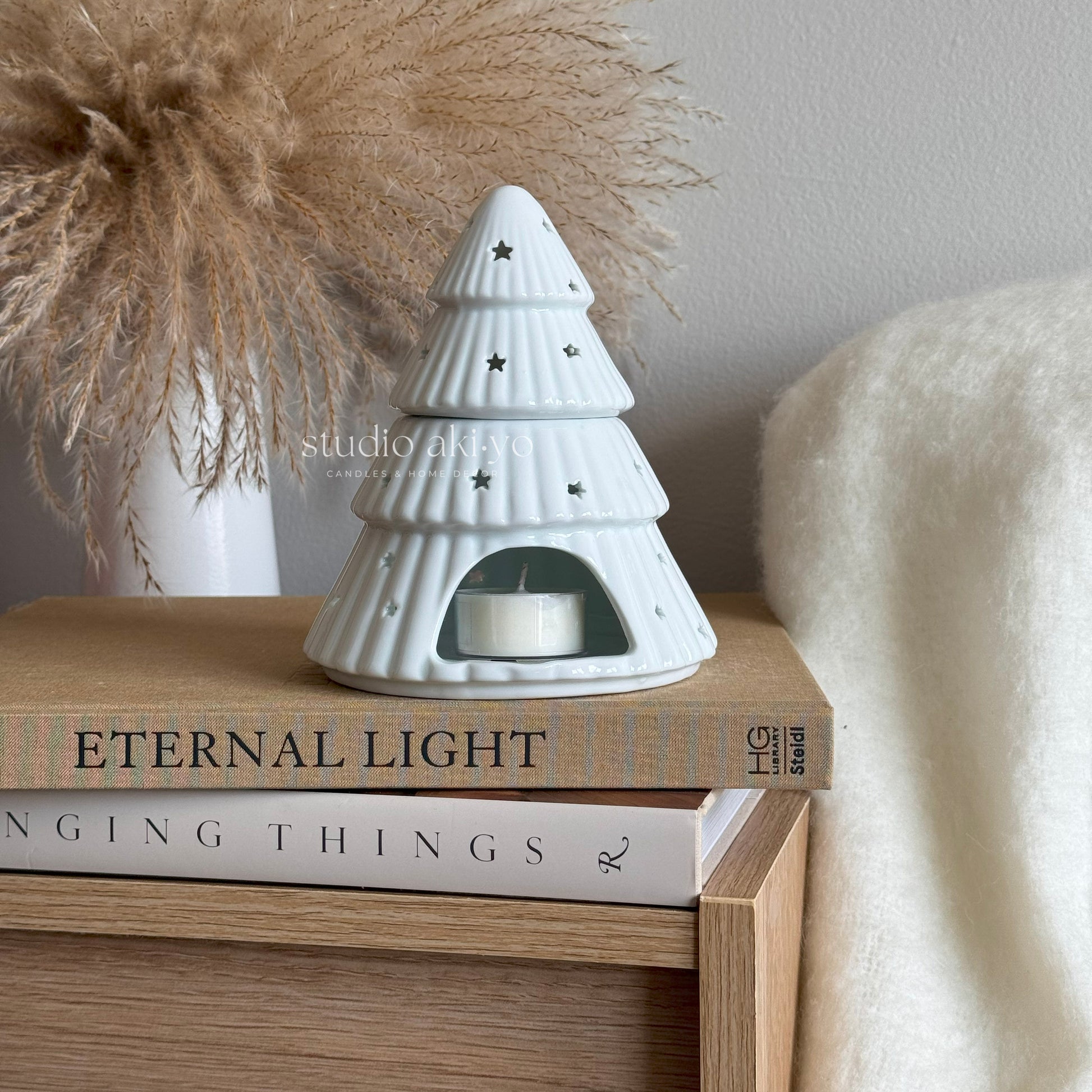 White ceramic tree-shaped candle holder on a stack of books with decorative items in the background.