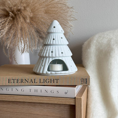 White ceramic tree-shaped candle holder on a stack of books with decorative items in the background.