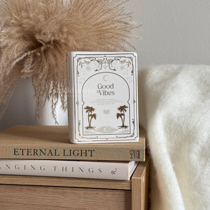 Stack of books with a decorative book titled 'Good Vibes' on top, against a neutral background.