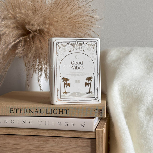 Stack of books with a decorative book titled 'Good Vibes' on top, against a neutral background.