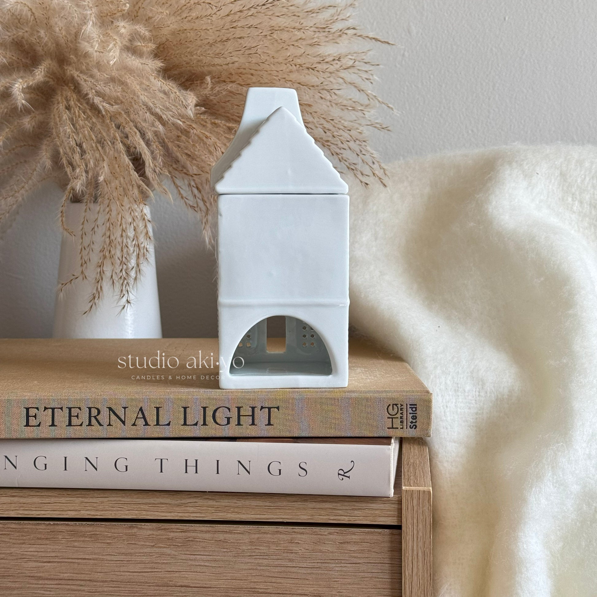 White decorative house on books with a vase and pampas grass in the background