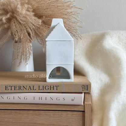 White decorative house on books with a vase and pampas grass in the background