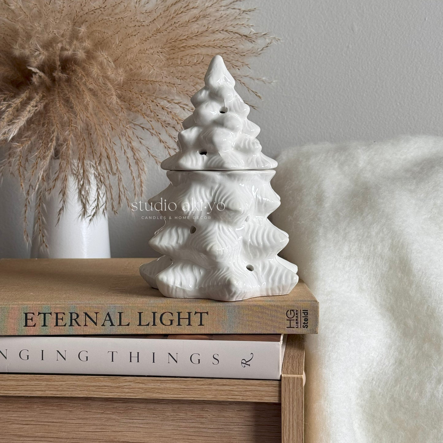 White ceramic Christmas tree ornament on a stack of books with a neutral background